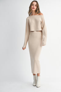Woman wearing a beige off-shoulder top and skirt set with white boots on a white background