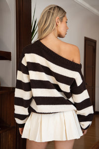 Woman wearing a brown and ivory striped sweater and white skirt indoors.